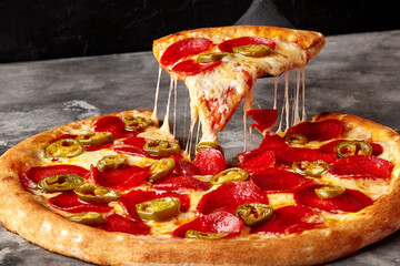 Slice of pizza with melted mozzarella, pepperoni and jalapeno on serving spatula
