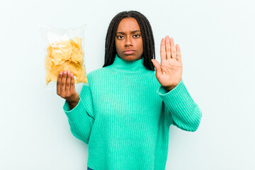 Young African American woman holding potato chips isolated on blue background standing with outstretched hand showing stop sign, preventing you.