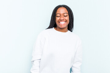 Fototapeta premium Young African American woman with braids hair isolated on blue background laughs and closes eyes, feels relaxed and happy.