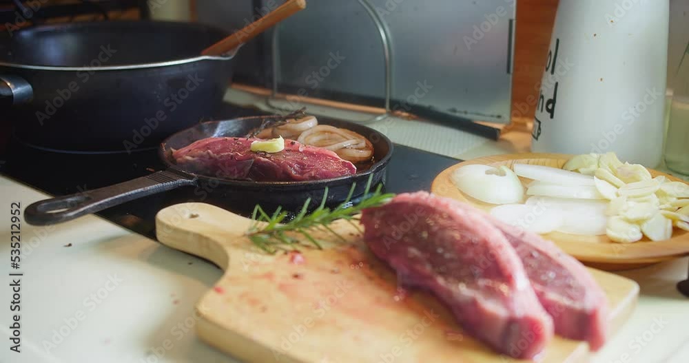 Wall mural Close up cooking meat beef steak on a hot grill pan with herbs in the kitchen, preparing barbeque grilling food at home