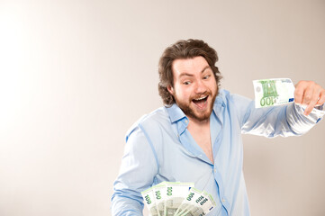 Portrait of happy caucasian man holding in hands 100 euro banknotes isolated over gray background