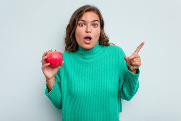 Young caucasian woman with an apple isolated on blue background having an idea, inspiration concept.