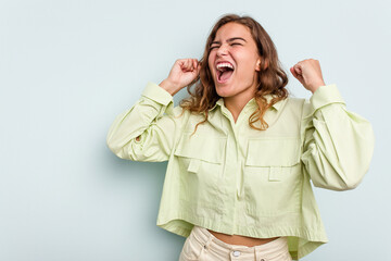 Young caucasian woman isolated on blue background raising fist after a victory, winner concept.