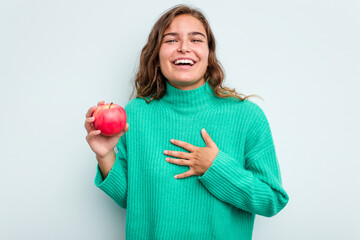 Young caucasian woman with an apple isolated on blue background laughs out loudly keeping hand on...
