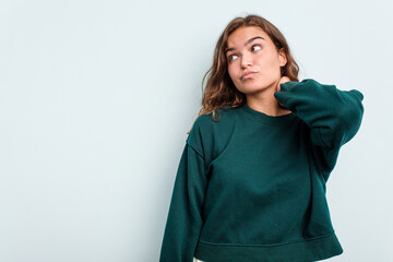 Young caucasian woman isolated on blue background touching back of head, thinking and making a choice.