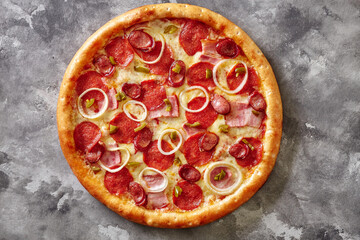 Pizza with bacon slices, salami, hunting sausages, jalapeno and onions on gray background