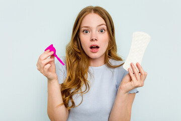 Young caucasian holding menstrual cup and sanitary napkin isolated on blue background