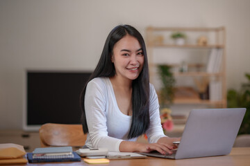 Beautiful Asian woman sitting intently working on a laptop computer at home.
