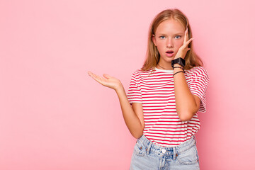 Caucasian teen girl isolated on pink background impressed holding copy space on palm.