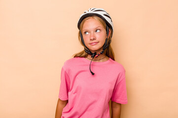 Little caucasian girl wearing a bike helmet isolated on beige background dreaming of achieving goals and purposes