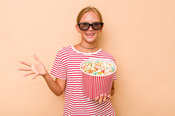 Little caucasian girl eating popcorn isolated on beige background receiving a pleasant surprise,...