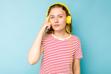 Young caucasian woman wearing headphones isolated on blue background pointing temple with finger, thinking, focused on a task.