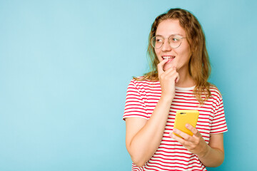 Young caucasian woman holding mobile phone isolated on blue background relaxed thinking about something looking at a copy space.