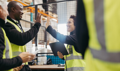Successful warehouse workers high fiving each other  and celebrating during a meeting