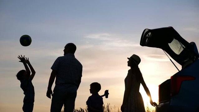 Schoolboy enjoying spending summer holidays with family throws ball to blue sky. Silhouettes of parents and younger brother look at boy and enjoy weekend
