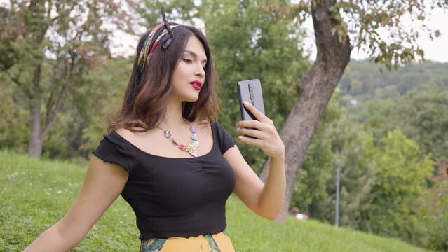 A young beautiful Caucasian woman takes selfies with a smartphone in a park on a sunny day
