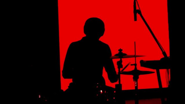 Male musician drummer plays drums on stage in a band. Black silhouette of a musician on a red background, close-up