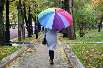 Rain in city, slim woman with colorful umbrella wearing grey coat walking down the street. Rainy weather in autumn park