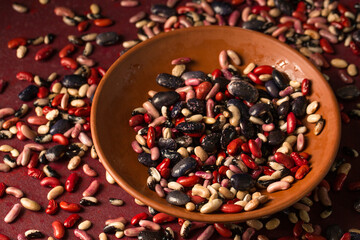 Ceramic bowl with beans on a burgundy background with scattered beans