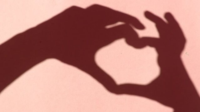 human hands making heart shadow on a red background.