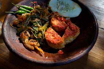 Tempeh Penyet typical Indonesian dish with chili sauce, cucumber and some vegetables in a traditional stone mortar