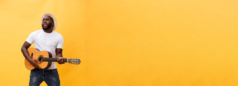 Full-length photo of excited artistic man playing his guitar in casual suite. Isolated on yellow background.