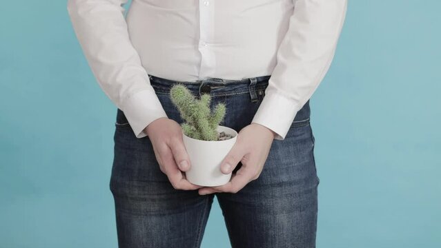 A man in a white shirt holds a pot of cactus in his hands against the background of the groin. The concept of chronic dysfunction in men. Psychosomatics in sexual problems