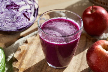 A glass of purple cabbage juice with a head of red cabbage and apples