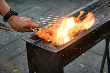 Malaysia, July 10, 2022 - Chicken skewers being cooked on an open fire at a night market.