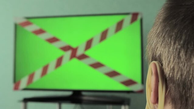 Hanging noodles on the ears of a man who watches TV with a forbidden tape and a green screen. The concept of misinformation, deceit and fakes