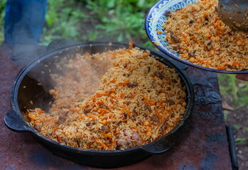 Cauldron and part of a colored plate with Uzbek pilaf close-up in summer