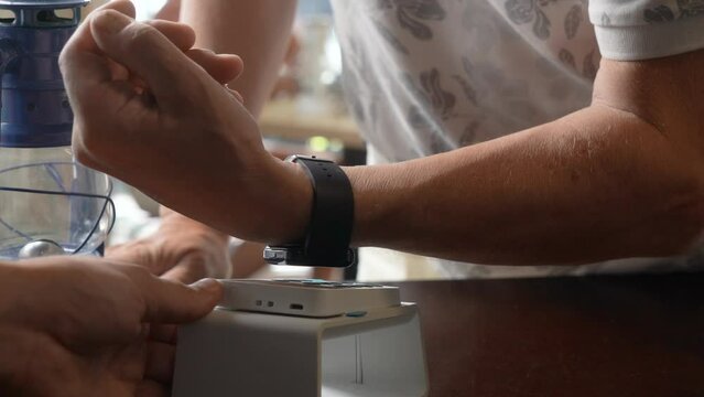 An elder man pay the bill with smart watch wirelessly on POS terminal using NFC contactless technology in a cafe. Purchase by smartwatch on electronic payment machine. E-money at cashless wallet.
