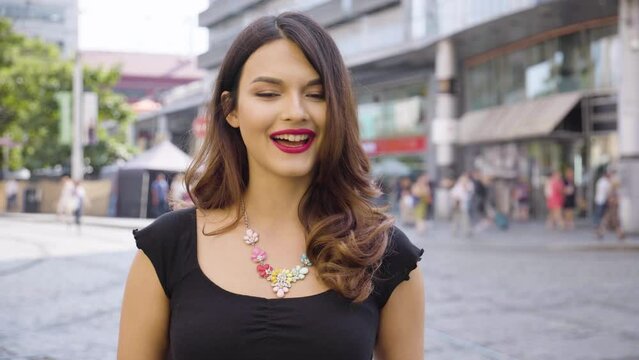 A young beautiful Caucasian woman talks to the camera with a smile in a street in an urban area
