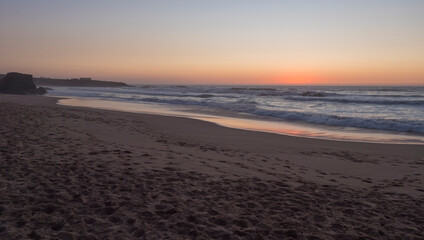 Sunset view of sand beach Praia Grande de Almograve with ocean waves in pink and red blue hour light, clear blue sky. Rota Vicentina coast, Almograve, Portugal