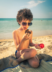 Hungry curly boy eating a tomato against the background of the sea. Sweet toddler child, eating meat and vegetables on the beach, kid enjoying delicious dinner at the beac