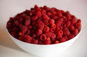 Fresh raspberries in a white bowl isolated on white table background