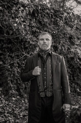 Vampire man wearing victorian suit in the autumn forest. Vintage medieval concept style. Black and...