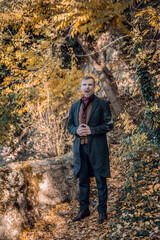Vampire man wearing victorian suit in the autumn forest. Vintage medieval concept style.