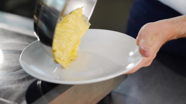 chef puts an omelette on a white plate in a loft-style kitchen