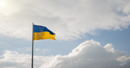 Ukraine independence patriotic concept of blue and yellow banner flagpole blowing on a wind with cloudy background scenic view with vibrant dramatic sun light, panoramic wallpaper picture