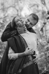 Vampire man wearing victorian suit in the autumn forest bites a woman. Vintage medieval concept style. Black and white photo