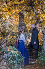 Vampire man wearing victorian suit with vampire woman in the autumn forest. Vintage medieval concept style.