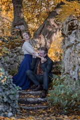 Vampire man wearing victorian suit in the autumn forest bites a woman. Vintage medieval concept style.