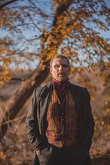 Vampire man wearing victorian suit in the autumn forest. Vintage medieval concept style.