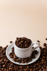 Espresso cup filled with coffee beans surrounded by a large number of coffee beans on a light beige background close-up.