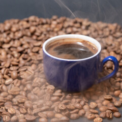 Roasted coffee and a cup of ready coffee on a dark background with light steam.