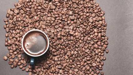 A cup of brewed black coffee on a dark background with beans.