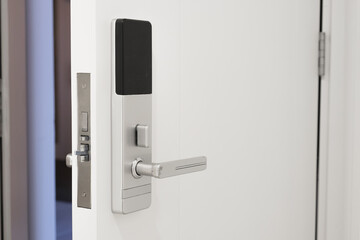 Slightly open white door to the hotel room with a Electronic magnetic lock. Electronic hotel lock with wireless reader. Chrome-plated handle on the interior door.