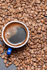 A cup of brewed black coffee on a dark background with beans.