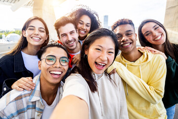 Diverse group of happy young best friends having fun taking selfie photo together - International...